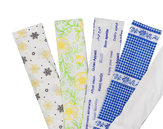 Five different paper napkins are arranged in a fan shape, each featuring a unique design, including snowflakes, yellow flowers, languages, a blue gingham pattern, and blue folk-style motifs on a white background.