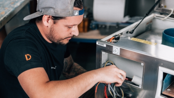 A technician works on a machine and connects cables in a workshop.