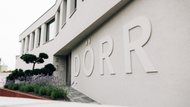 Modernes Gebäude mit großem Schriftzug "DÖRR" und bepflanztem Vorbereich