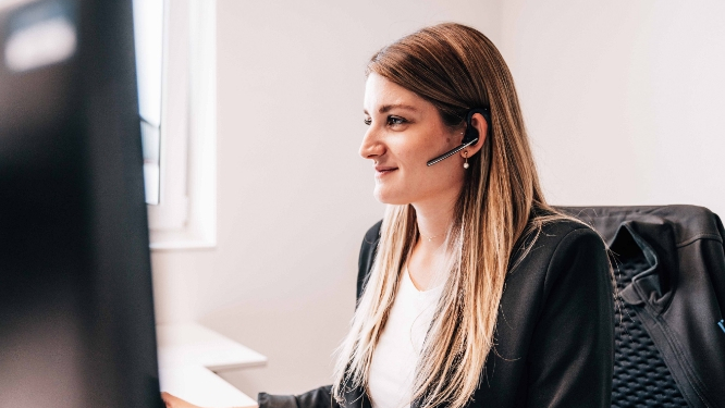 Eine Frau mit Headset sitzt am Computer und lächelt