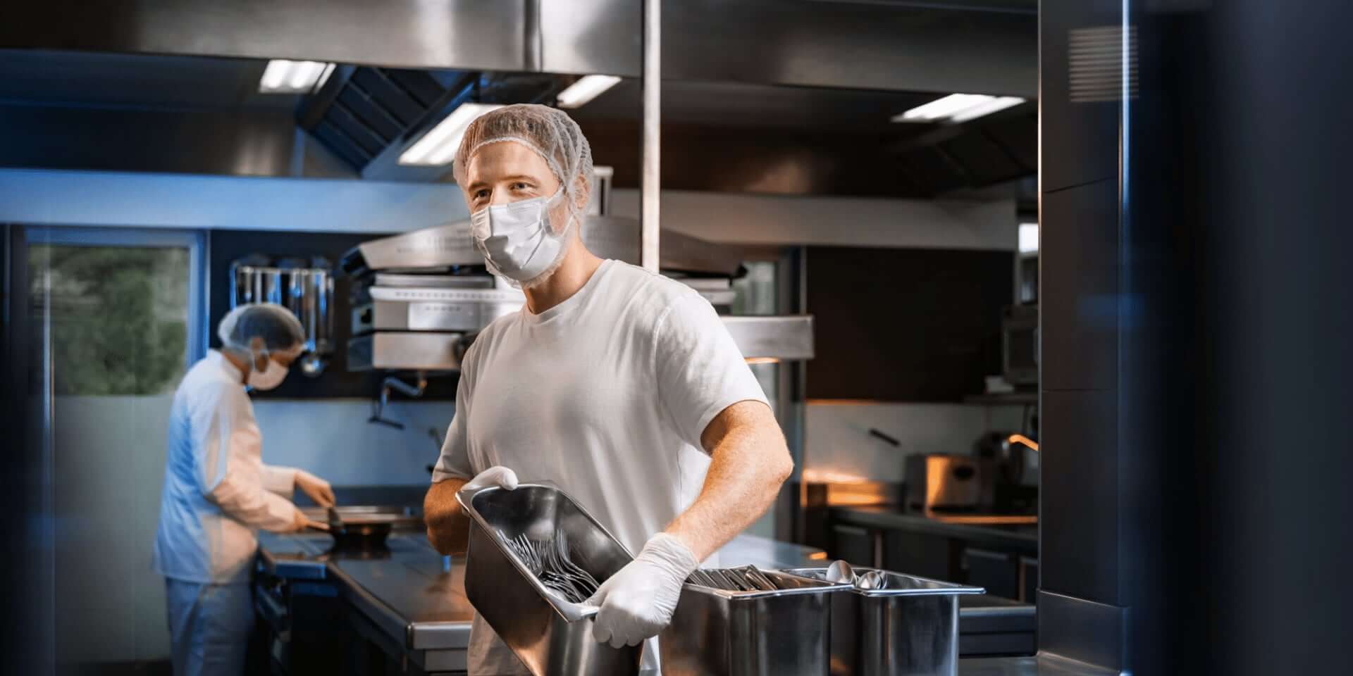 Mann mit Mundschutz und Edelstahlkiste mit Gabeln in der Hand