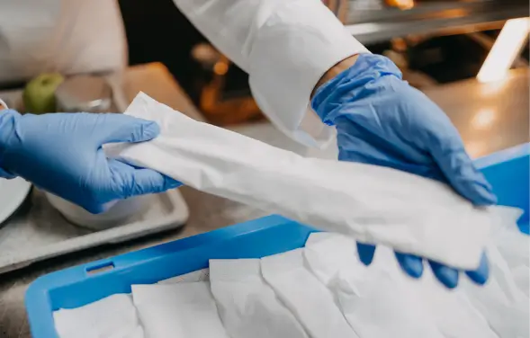 Person mit Gummihandschuhen hält eine Verpackung für Besteck.