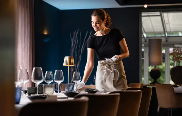 Frau deckt einen Esstisch in elegantem Ambiente.