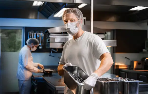 Mann trägt einen Behälter mit Besteck in einer professionellen Großküche.