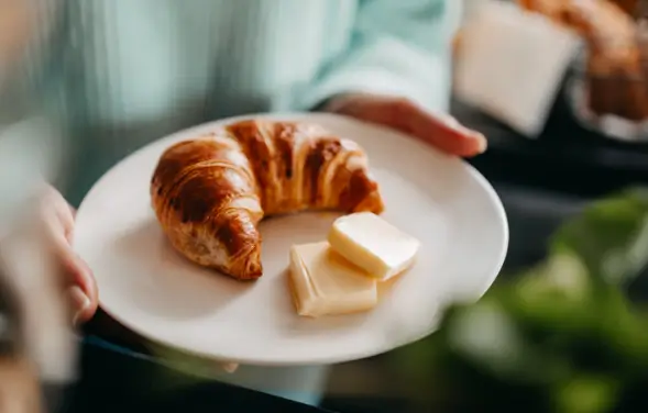 Teller in einer Hand mit einem Croissant und zwei Portionen Butter aus dem EasyButter Pro.