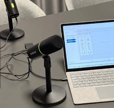 Bild von einem Tisch mit Laptop und zwei Stand Podcast Mikrofonen. Zudem ein Titelbild eines Podcasts.